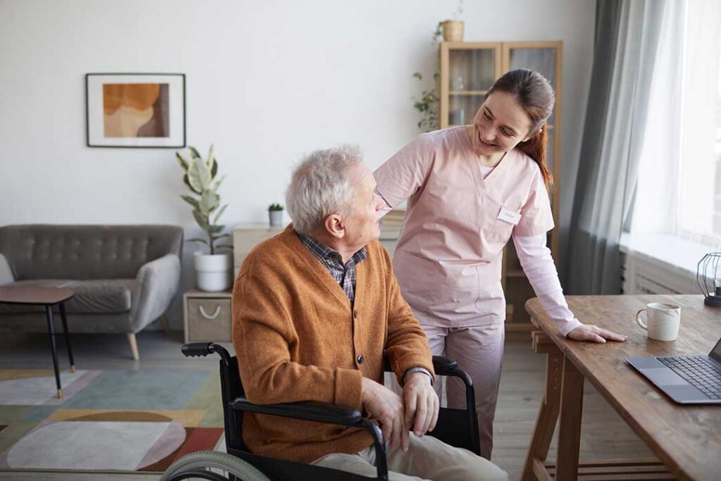 Care staff and an older adult reviewing medication and health documents together at a kitchen table.